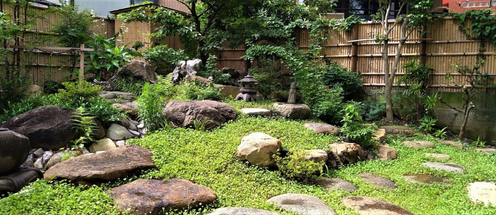 Asiatisk inredning av en mellanstor trädgård framför huset, med naturstensplattor