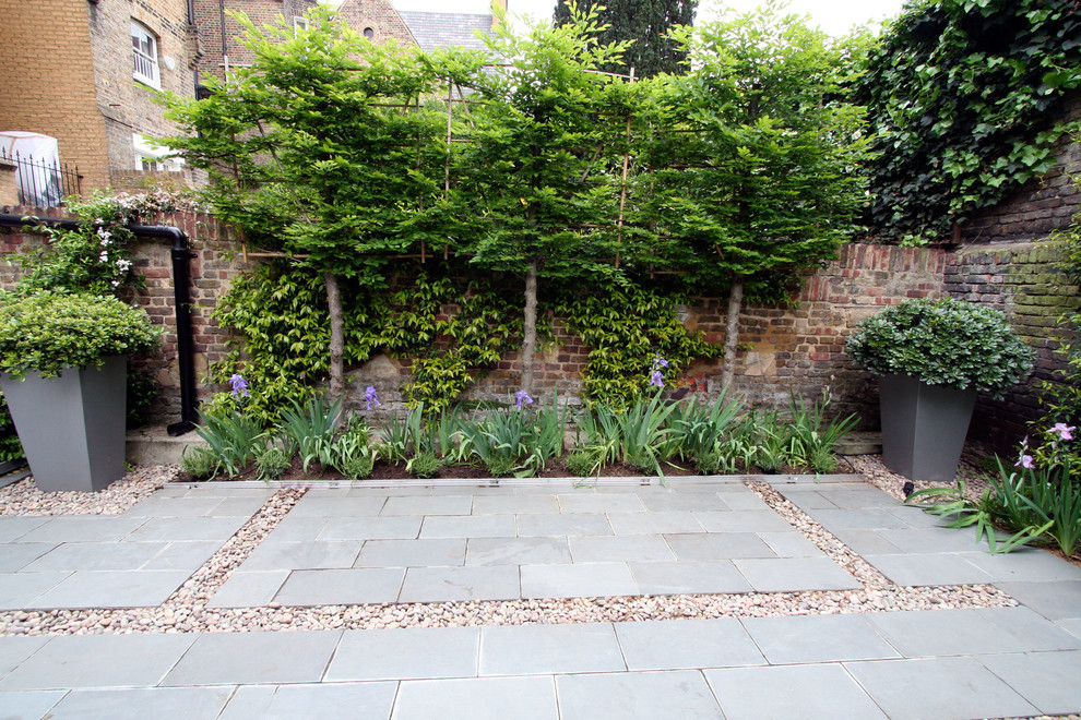 This is an example of a contemporary backyard patio in London with natural stone pavers.