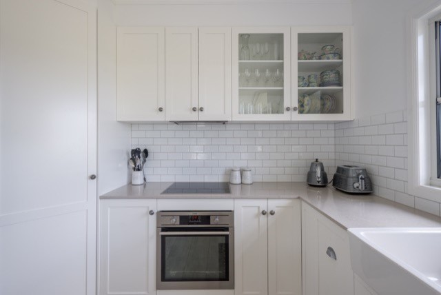 Photo of a mid-sized transitional u-shaped eat-in kitchen in Brisbane with a farmhouse sink, white splashback, subway tile splashback, stainless steel appliances and light hardwood floors.