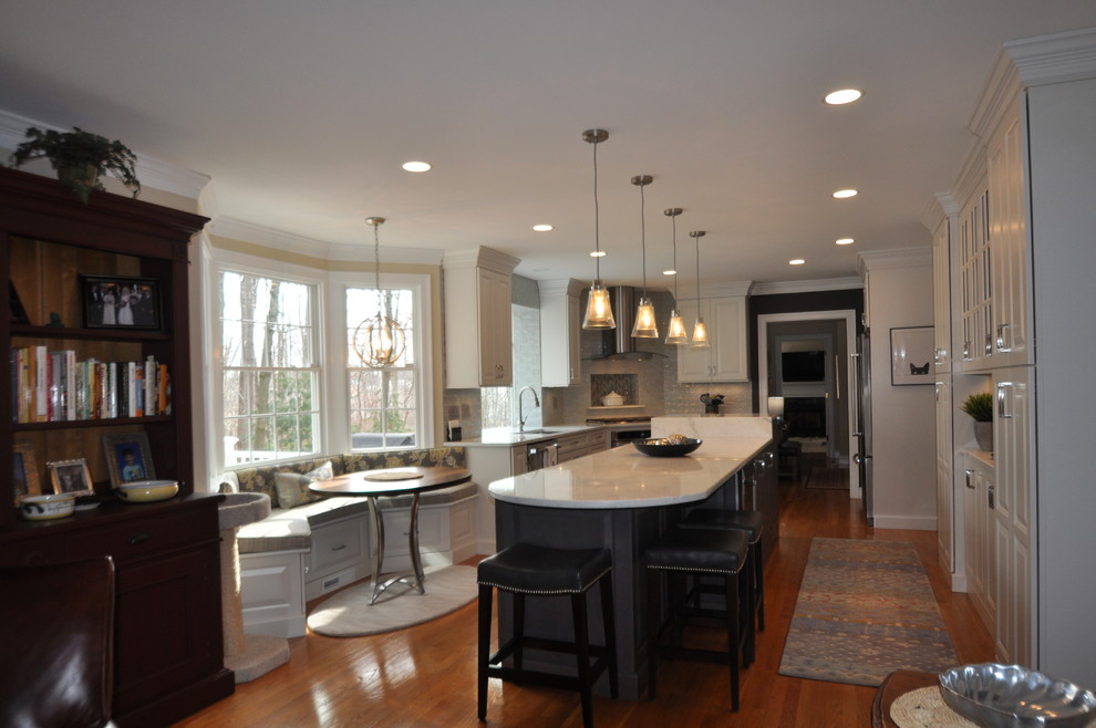 Mid-sized transitional l-shaped open plan kitchen in Boston with an undermount sink, raised-panel cabinets, white cabinets, quartz benchtops, grey splashback, porcelain splashback, stainless steel appliances, medium hardwood floors, with island, brown floor and white benchtop.