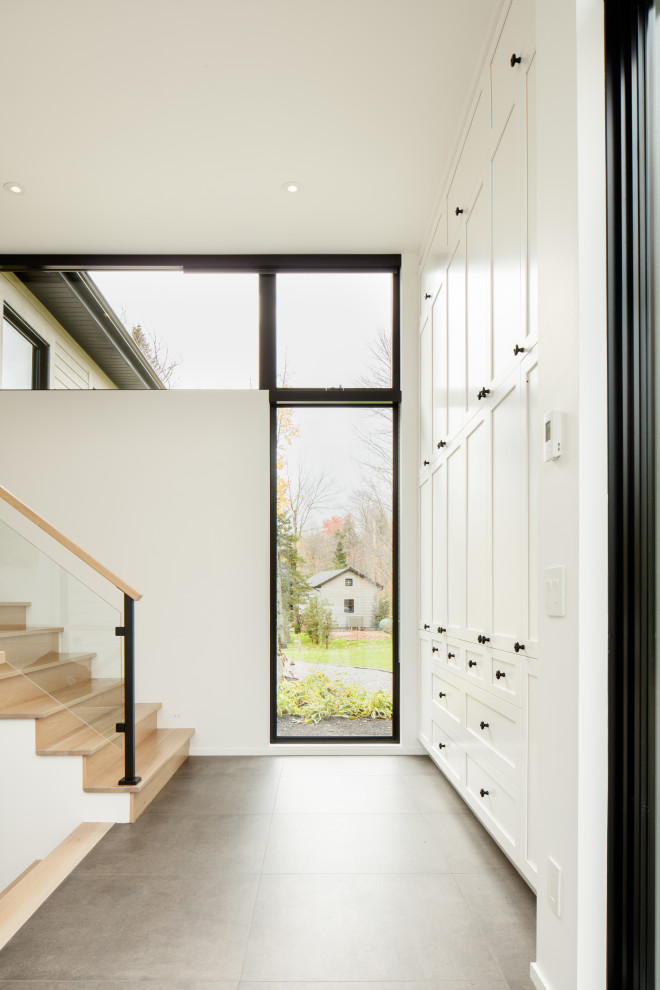 Cette image montre une grande entrée design avec un vestiaire, un mur blanc, un sol en carrelage de céramique, une porte simple, une porte en verre, un sol gris et du lambris.