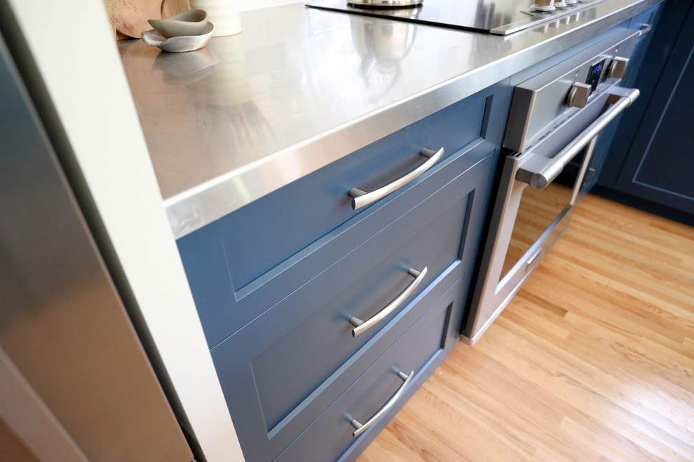 Inspiration for a mid-sized transitional l-shaped light wood floor and beige floor open concept kitchen remodel with an integrated sink, shaker cabinets, blue cabinets, stainless steel countertops, ceramic backsplash, stainless steel appliances, an island and gray countertops
