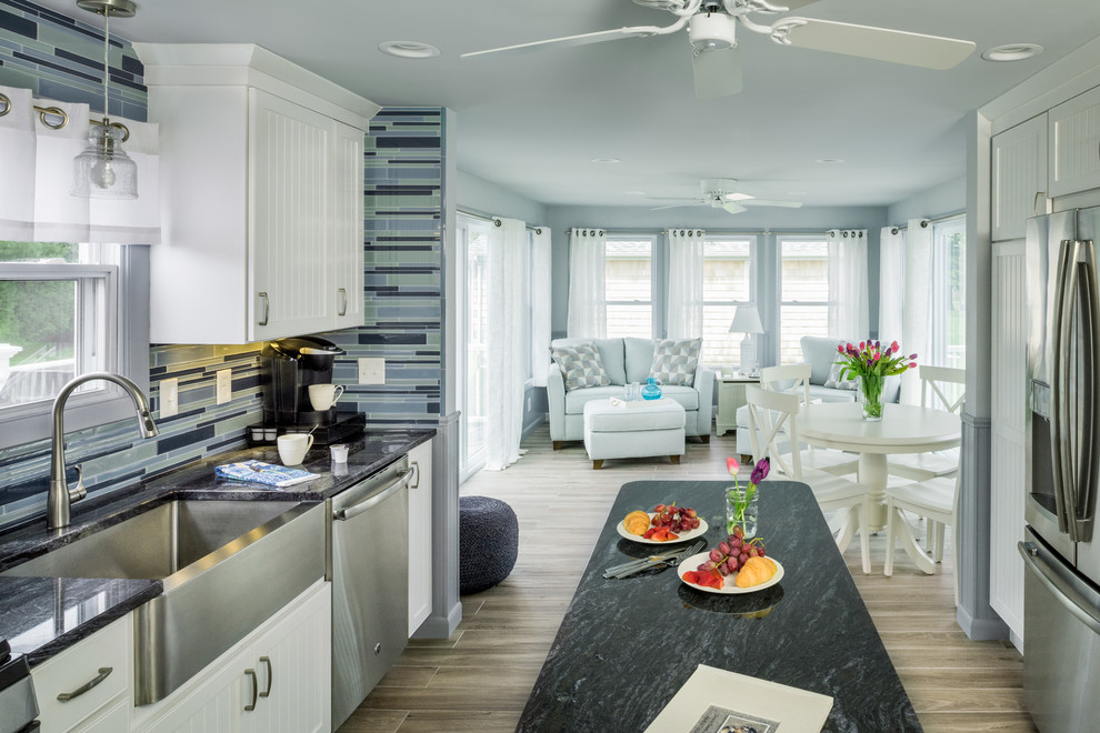 Design ideas for a small beach style galley eat-in kitchen in Providence with a farmhouse sink, recessed-panel cabinets, white cabinets, granite benchtops, blue splashback, glass tile splashback, stainless steel appliances, porcelain floors, with island and grey floor.