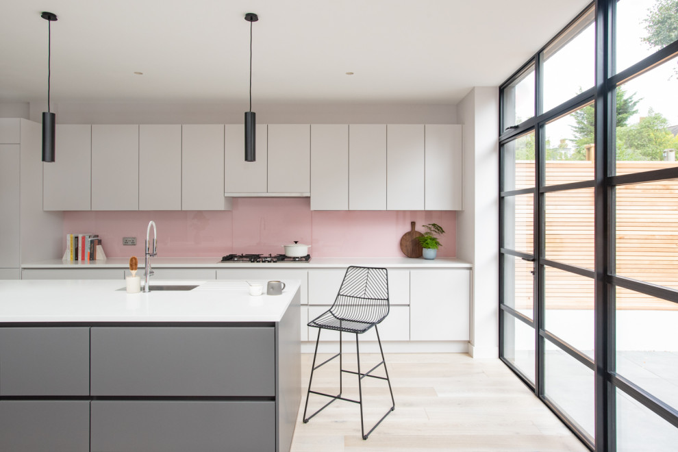 Photo of a mid-sized contemporary kitchen in London with flat-panel cabinets, quartzite benchtops, pink splashback, glass sheet splashback, light hardwood floors, with island, white benchtop, a single-bowl sink, white cabinets and beige floor.