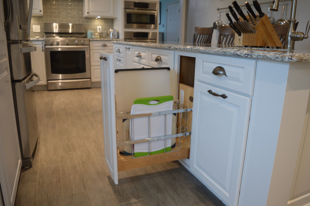 Example of a large transitional u-shaped ceramic tile and gray floor home design design with a farmhouse sink, raised-panel cabinets, white cabinets, quartz countertops, gray backsplash, glass tile backsplash, stainless steel appliances and an island