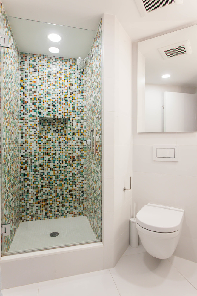 Mid-sized contemporary kids bathroom in New York with white cabinets, a corner shower, a wall-mount toilet, multi-coloured tile, glass tile, white walls, porcelain floors, recycled glass benchtops, white floor and a hinged shower door.