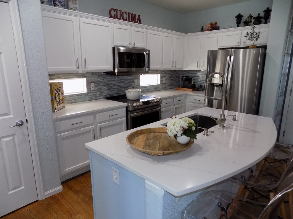 Bild på ett litet funkis vit vitt u-kök, med en undermonterad diskho, luckor med infälld panel, vita skåp, bänkskiva i kvartsit, blått stänkskydd, stänkskydd i glaskakel, rostfria vitvaror, målat trägolv, en köksö och gult golv