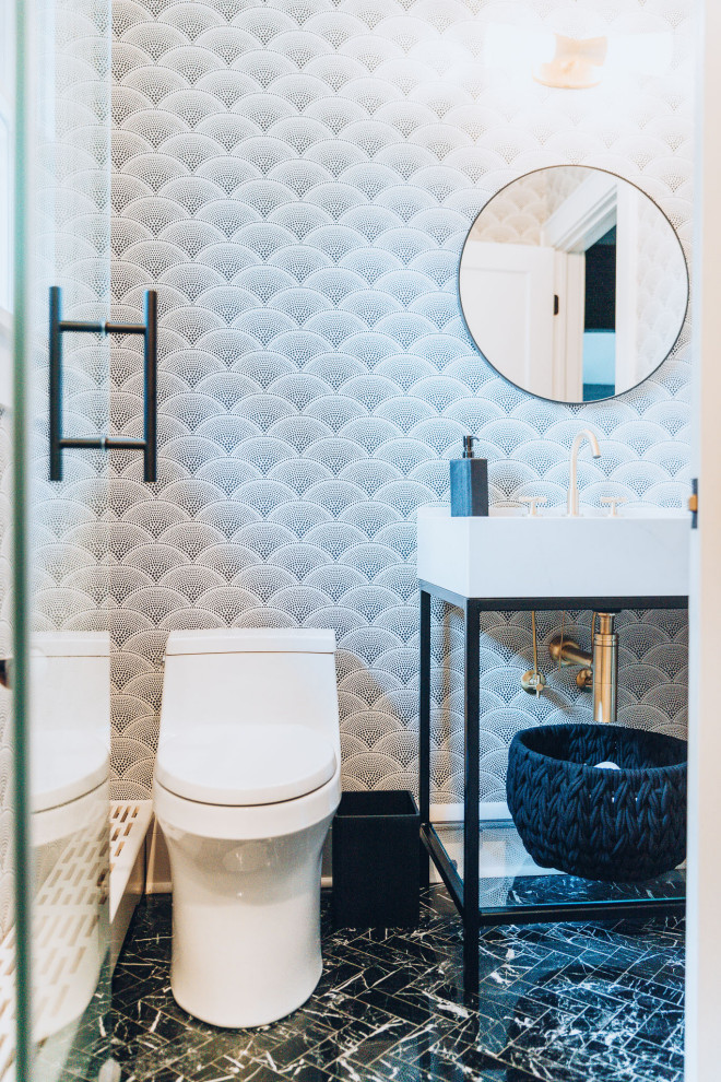 Photo of a mid-sized modern kids bathroom in New York with white cabinets, an alcove shower, a one-piece toilet, gray tile, ceramic tile, multi-coloured walls, ceramic floors, a pedestal sink, marble benchtops, black floor, a hinged shower door, white benchtops, a single vanity, a freestanding vanity, coffered and wallpaper.
