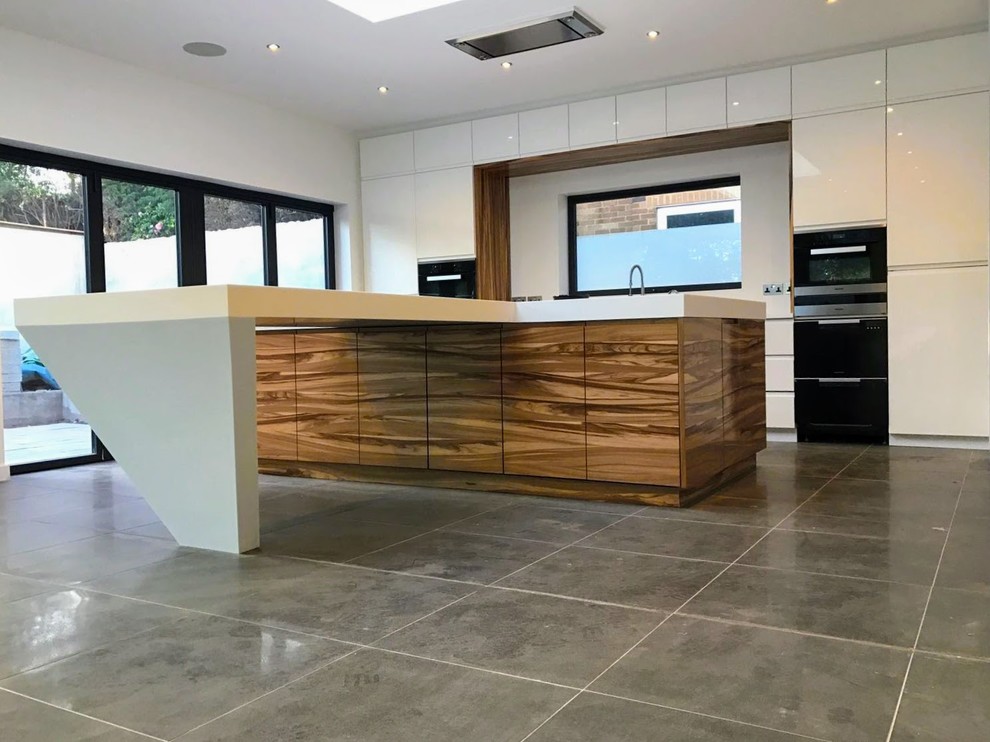Photo of a large contemporary single-wall open plan kitchen in West Midlands with an integrated sink, glass-front cabinets, white cabinets, solid surface benchtops, white splashback, window splashback, panelled appliances, porcelain floors and with island.