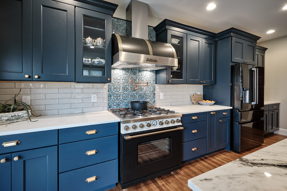 Inspiration for a large eclectic galley open plan kitchen in Philadelphia with a farmhouse sink, recessed-panel cabinets, blue cabinets, quartzite benchtops, grey splashback, ceramic splashback, black appliances, medium hardwood floors, with island, brown floor and multi-coloured benchtop.