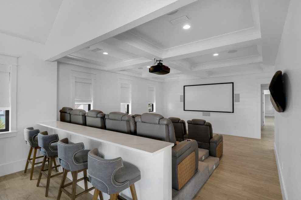 Large nautical enclosed home cinema in Other with white walls, light hardwood flooring, a projector screen and brown floors.