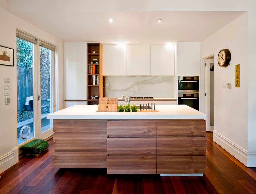 This is an example of a mid-sized contemporary galley kitchen in Melbourne with a double-bowl sink, white splashback, stone slab splashback, stainless steel appliances, dark hardwood floors, with island, flat-panel cabinets and medium wood cabinets.