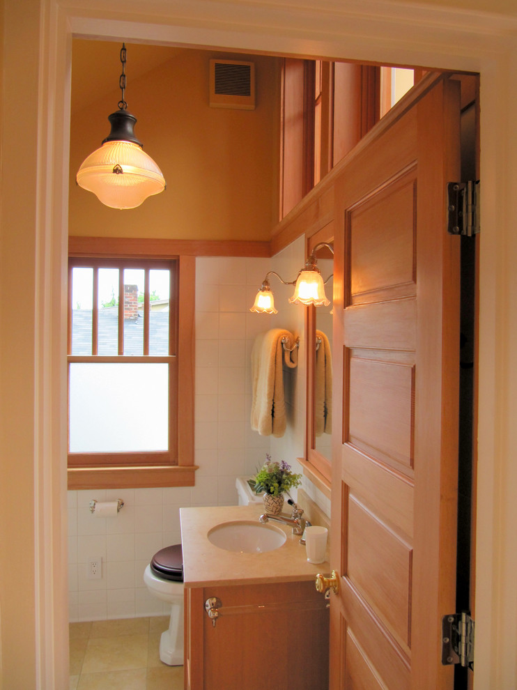 Inspiration for a small arts and crafts 3/4 bathroom in Seattle with recessed-panel cabinets, medium wood cabinets, an alcove shower, a two-piece toilet, white tile, ceramic tile, orange walls, limestone floors, a drop-in sink and limestone benchtops.