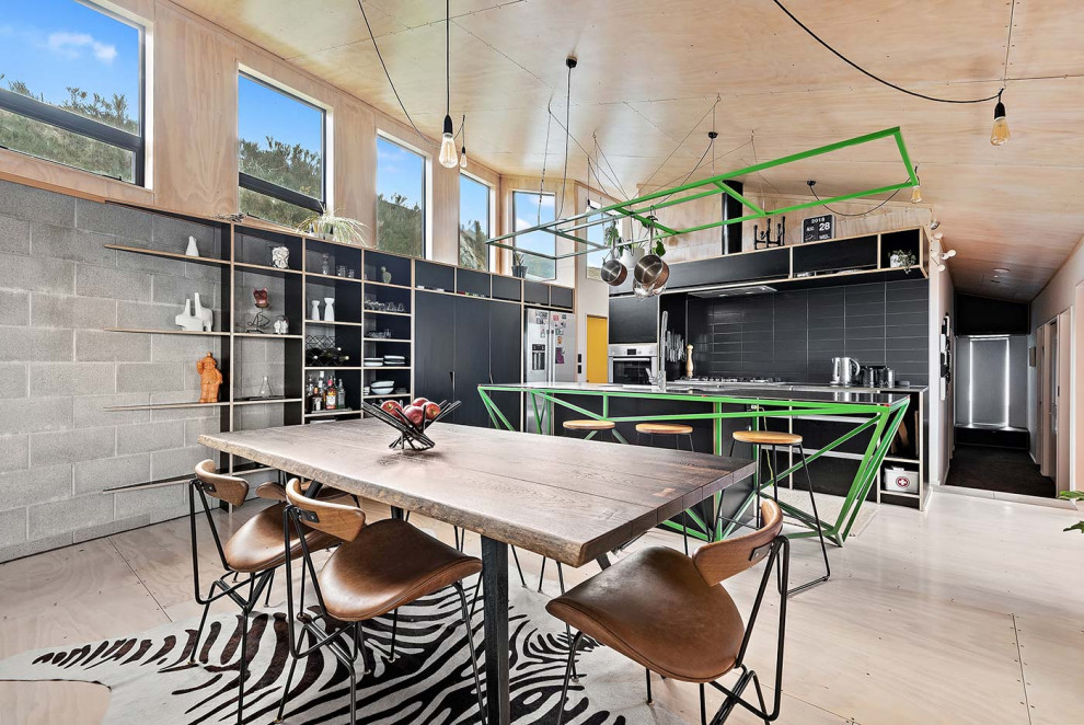 Mid-sized industrial galley eat-in kitchen in Wellington with an integrated sink, recessed-panel cabinets, black cabinets, stainless steel benchtops, black splashback, ceramic splashback, stainless steel appliances, plywood floors, with island and timber.