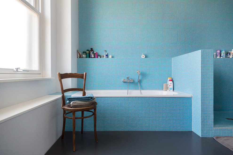 This is an example of a large industrial bathroom in Berlin with a drop-in tub, an alcove shower, blue tile, mosaic tile and white walls.