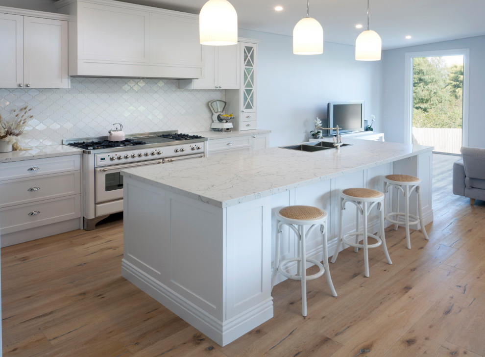Idéer för ett stort klassiskt grå kök med öppen planlösning, med en dubbel diskho, skåp i shakerstil, vita skåp, bänkskiva i kvarts, vitt stänkskydd, stänkskydd i keramik, vita vitvaror, ljust trägolv, en köksö och brunt golv