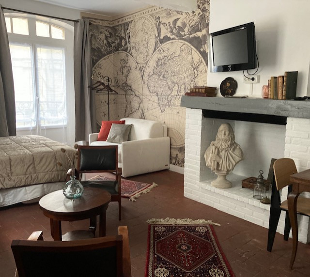 Kleines, Abgetrenntes Wohnzimmer ohne Kamin mit weißer Wandfarbe, Terrakottaboden, Kaminumrandung aus Holz, TV-Wand, rotem Boden, freigelegten Dachbalken und Tapetenwänden in Korsika