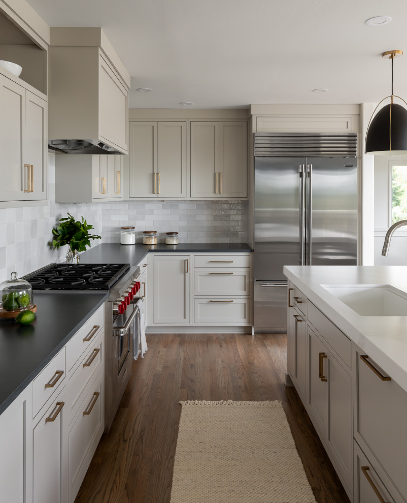 Example of a mid-sized transitional l-shaped medium tone wood floor and brown floor open concept kitchen design in Seattle with an undermount sink, shaker cabinets, gray cabinets, quartz countertops, white backsplash, subway tile backsplash, stainless steel appliances, an island and black countertops