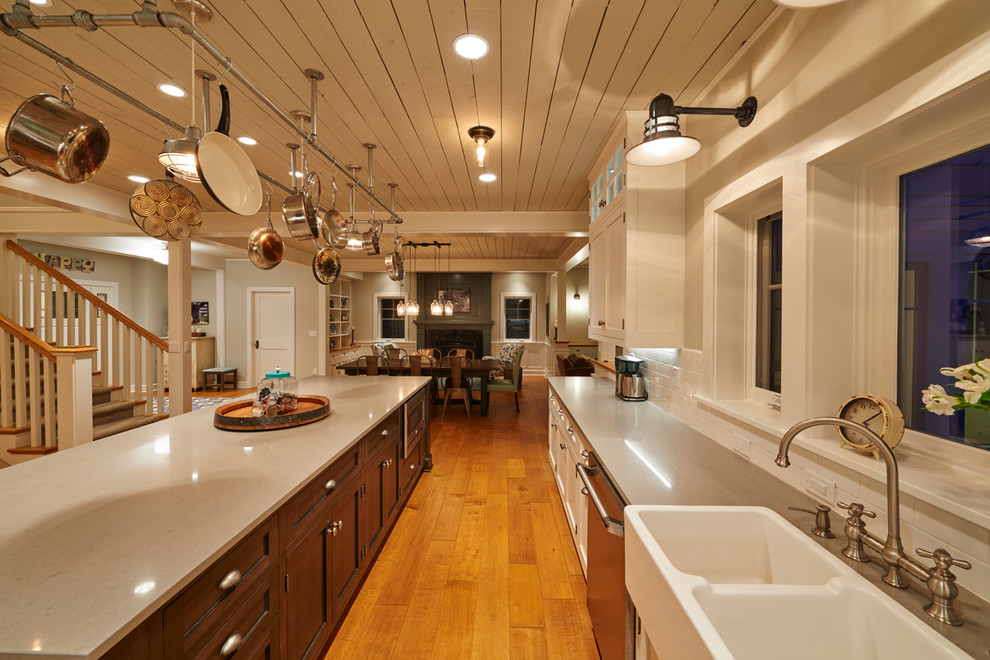 Photo of a mid-sized country single-wall separate kitchen in Seattle with a farmhouse sink, recessed-panel cabinets, white cabinets, quartz benchtops, white splashback, subway tile splashback, stainless steel appliances, light hardwood floors, with island and beige floor.