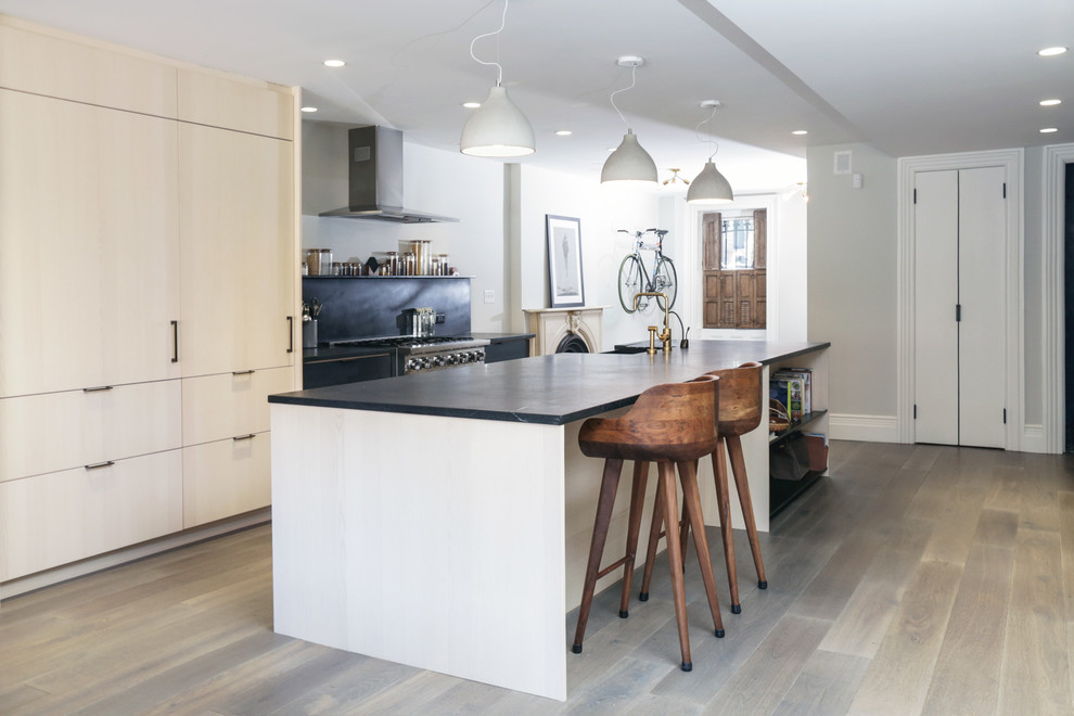 This is an example of a large contemporary open plan kitchen in New York with flat-panel cabinets, light wood cabinets, marble benchtops, black splashback, stainless steel appliances, dark hardwood floors, with island, grey floor and a farmhouse sink.