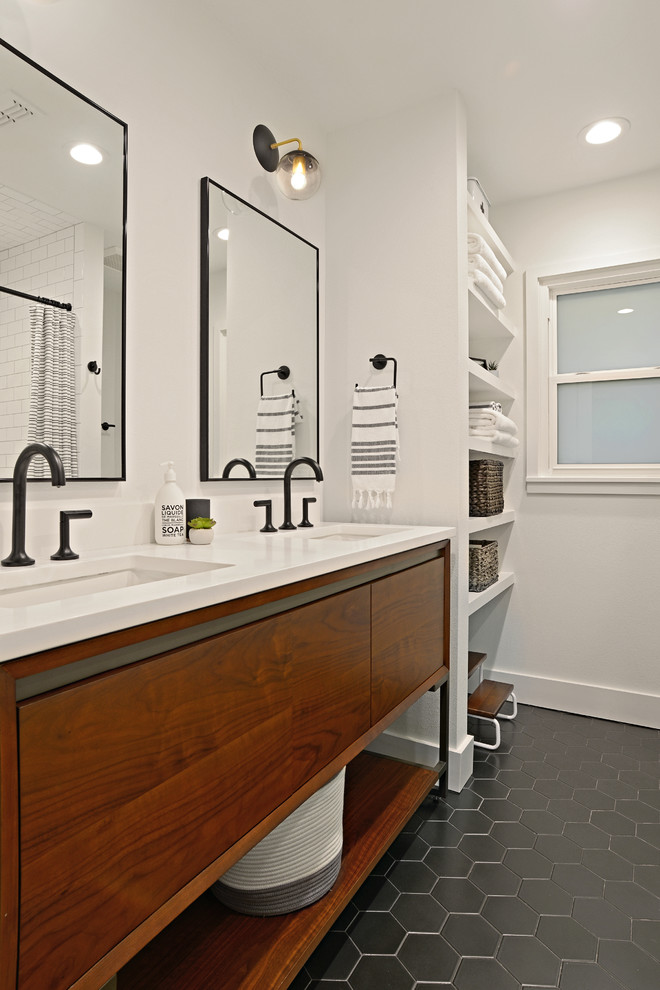 Photo of a mid-sized midcentury kids bathroom in Dallas with flat-panel cabinets, medium wood cabinets, an alcove tub, a shower/bathtub combo, a two-piece toilet, white tile, ceramic tile, white walls, porcelain floors, an undermount sink, engineered quartz benchtops, black floor, a shower curtain, white benchtops, a double vanity and a freestanding vanity.