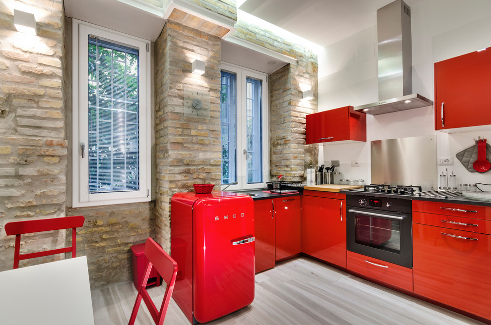 This is an example of a mid-sized contemporary l-shaped eat-in kitchen in Rome with flat-panel cabinets, red cabinets, metallic splashback, metal splashback, black appliances and medium hardwood floors.