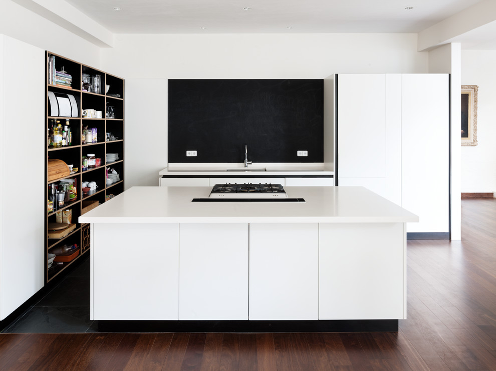 Photo of a small contemporary open plan kitchen in Berlin with flat-panel cabinets, white cabinets, solid surface benchtops, black splashback, with island, a single-bowl sink and dark hardwood floors.