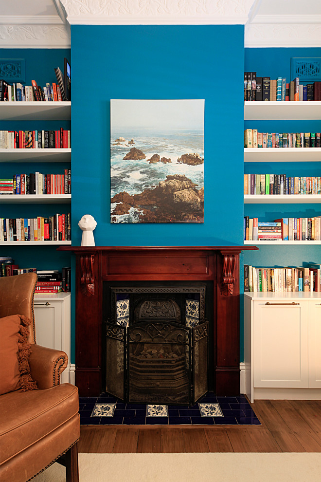 Imagen de habitación de invitados tradicional renovada pequeña con paredes azules, suelo de madera en tonos medios, todas las chimeneas, marco de chimenea de madera y suelo marrón
