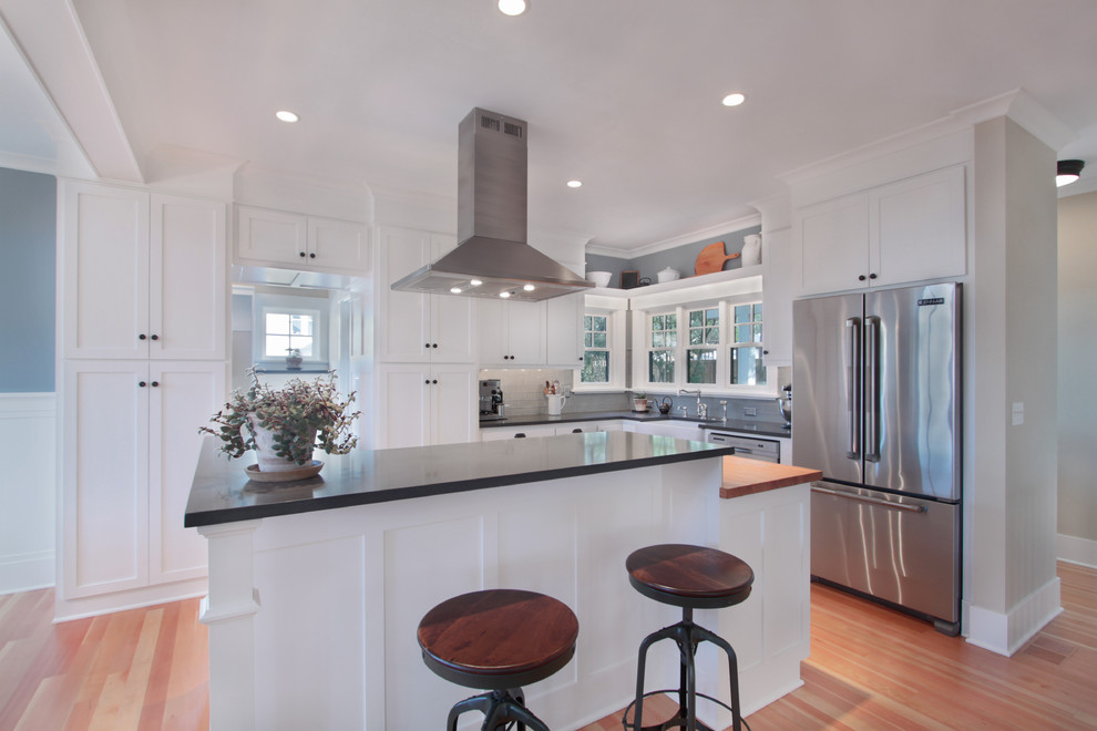 This is an example of a mid-sized arts and crafts l-shaped eat-in kitchen in Seattle with an undermount sink, shaker cabinets, white cabinets, quartzite benchtops, white splashback, glass tile splashback, stainless steel appliances, medium hardwood floors, with island, brown floor and grey benchtop.