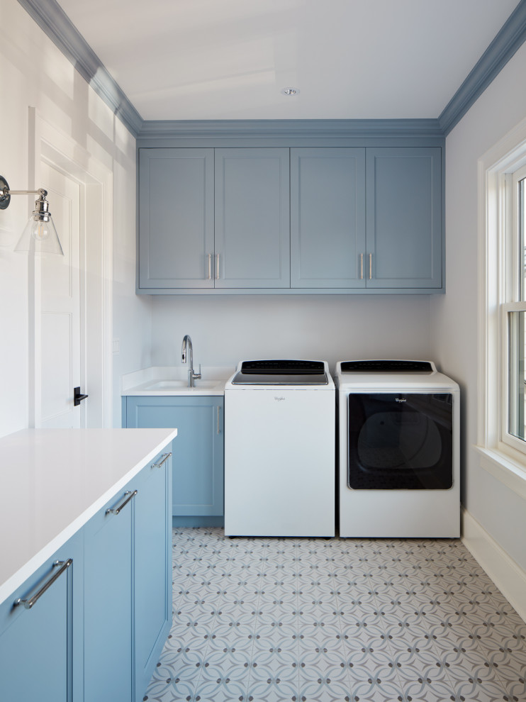Photo of a transitional laundry room in Chicago with an undermount sink, recessed-panel cabinets, blue cabinets, solid surface benchtops, porcelain floors, a side-by-side washer and dryer, blue floor and white benchtop.