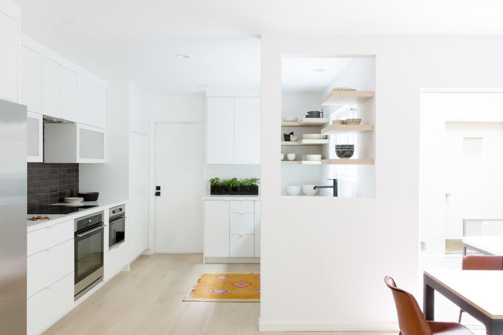 Inspiration for a mid-sized scandinavian l-shaped open plan kitchen in Los Angeles with flat-panel cabinets, white cabinets, quartz benchtops, white splashback, ceramic splashback, stainless steel appliances, light hardwood floors, no island and beige floor.
