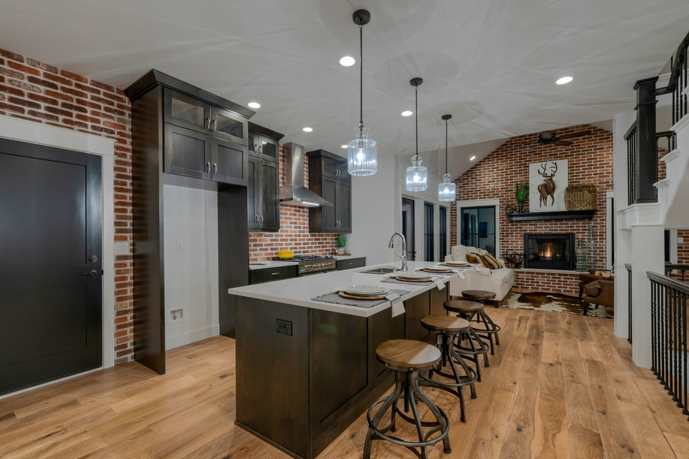 Mid-sized industrial single-wall open plan kitchen in Denver with shaker cabinets, dark wood cabinets, with island, a double-bowl sink, quartz benchtops, brown splashback, brick splashback, stainless steel appliances, medium hardwood floors, brown floor and white benchtop.