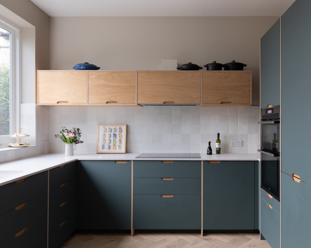 This is an example of a medium sized contemporary u-shaped enclosed kitchen in London with a built-in sink, flat-panel cabinets, green cabinets, quartz worktops, white splashback, ceramic splashback, white appliances, light hardwood flooring, no island, beige floors and white worktops.