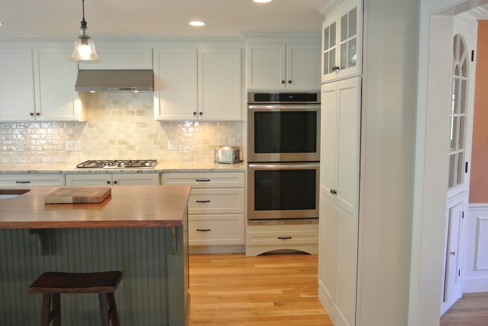 Example of a transitional galley light wood floor eat-in kitchen design in Boston with an undermount sink, stainless steel appliances, an island, shaker cabinets, white cabinets, wood countertops, white backsplash, ceramic backsplash and brown countertops