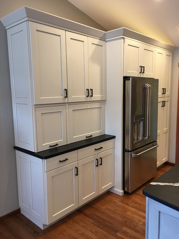 Example of a large transitional l-shaped dark wood floor and brown floor eat-in kitchen design with a farmhouse sink, shaker cabinets, white cabinets, quartz countertops, gray backsplash, stainless steel appliances and an island