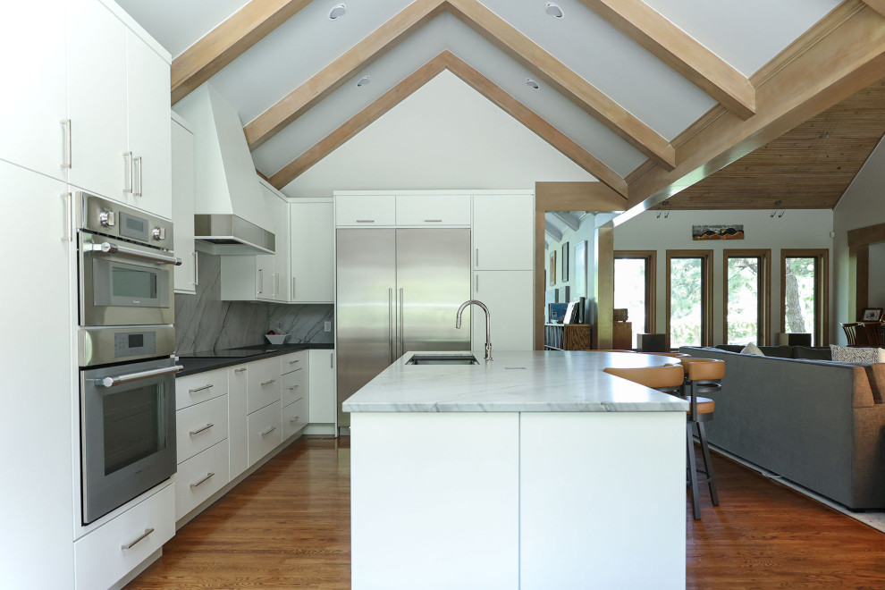 Open concept kitchen - mid-sized transitional u-shaped medium tone wood floor, brown floor and vaulted ceiling open concept kitchen idea with an undermount sink, flat-panel cabinets, white cabinets, quartzite countertops, gray backsplash, marble backsplash, stainless steel appliances, an island and gray countertops