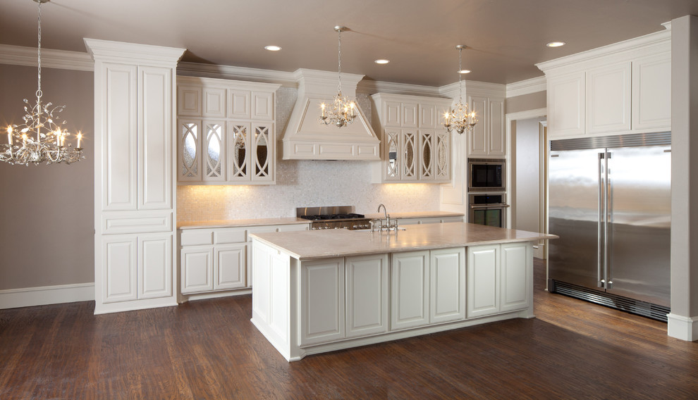 Inspiration for a mid-sized traditional single-wall kitchen in Oklahoma City with a farmhouse sink, raised-panel cabinets, white cabinets, marble benchtops, white splashback, mosaic tile splashback, stainless steel appliances, medium hardwood floors and with island.