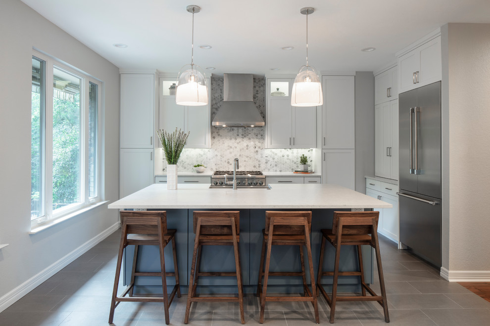 This is an example of a transitional l-shaped kitchen in Austin with a farmhouse sink, shaker cabinets, white cabinets, white splashback, stainless steel appliances, with island, grey floor and white benchtop.