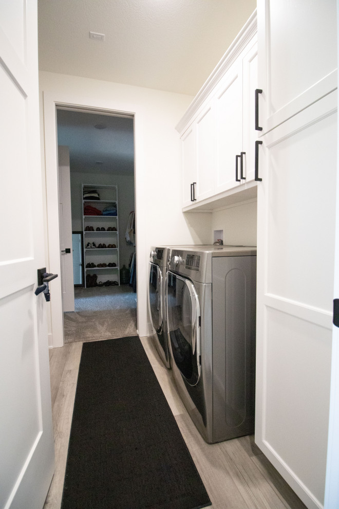 This is an example of a modern galley separated utility room in Omaha with a built-in sink, shaker cabinets, white cabinets, white walls and a side by side washer and dryer.