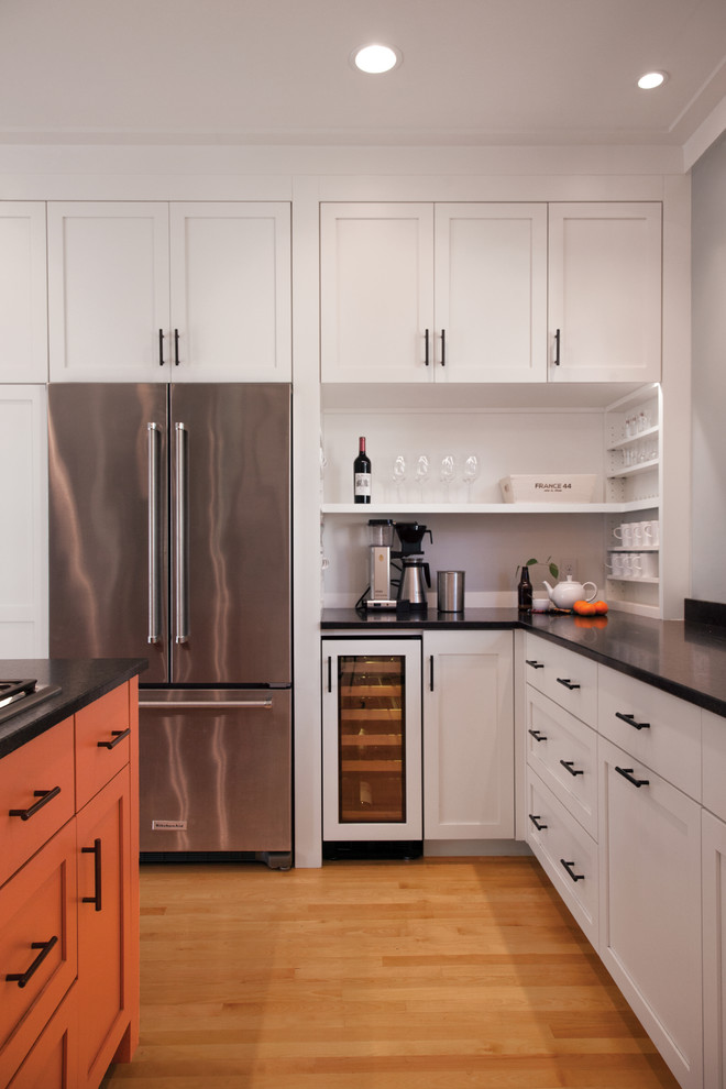 This is an example of a mid-sized transitional u-shaped kitchen in Minneapolis with an undermount sink, shaker cabinets, orange cabinets, solid surface benchtops, stainless steel appliances, medium hardwood floors, with island, brown floor and black benchtop.