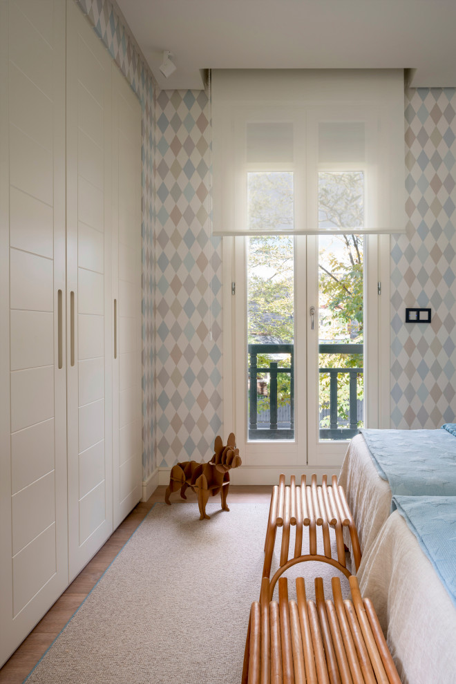 This is an example of a large classic gender neutral children’s room in Bilbao with multi-coloured walls, laminate floors, brown floors and wallpapered walls.