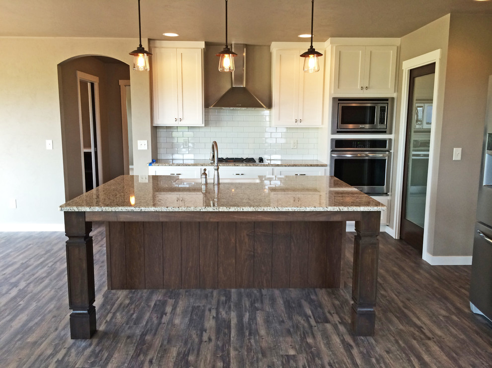 This is an example of a large arts and crafts open plan kitchen in Milwaukee with a farmhouse sink, shaker cabinets, white cabinets, granite benchtops, white splashback, subway tile splashback, stainless steel appliances, vinyl floors and with island.