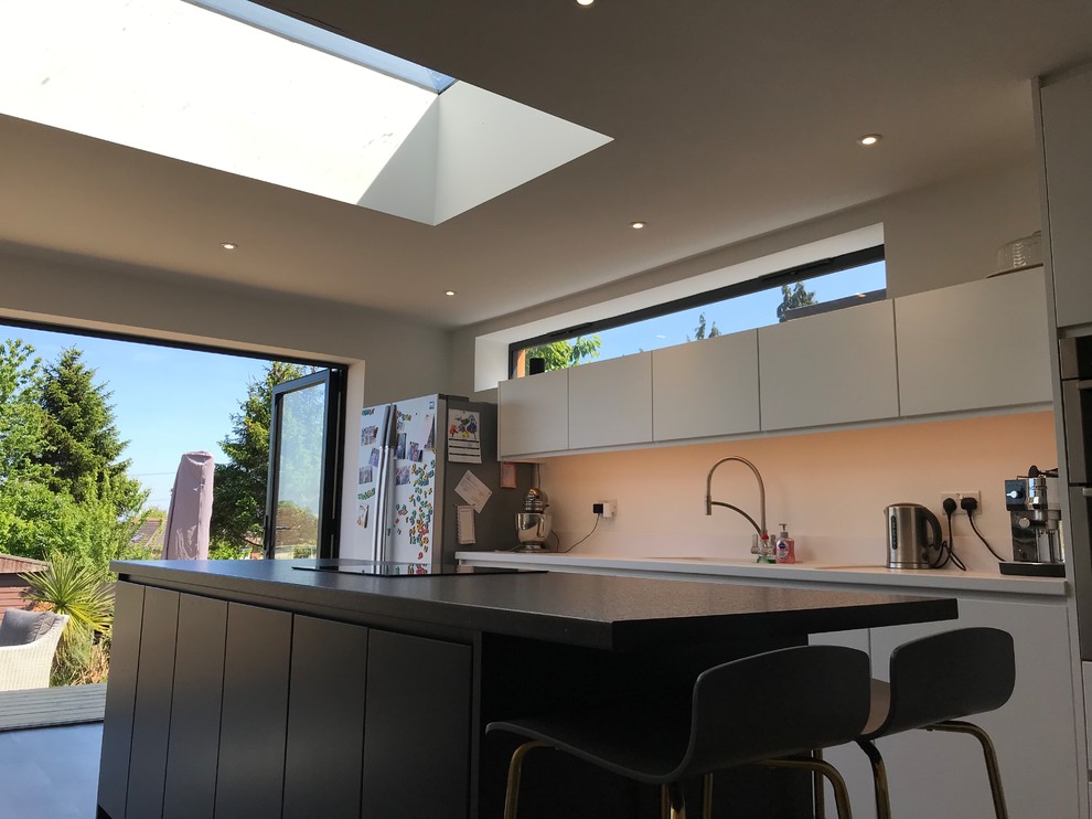 Photo of a small contemporary galley kitchen in Hampshire with an undermount sink, flat-panel cabinets, white cabinets, solid surface benchtops, white splashback, with island, grey floor and black benchtop.