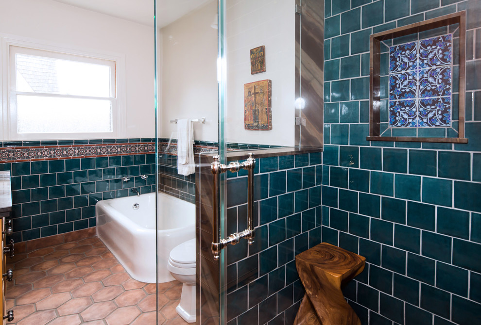Photo of a mid-sized mediterranean master bathroom in Los Angeles with an undermount sink, shaker cabinets, medium wood cabinets, quartzite benchtops, a corner tub, a corner shower, a one-piece toilet, blue tile, ceramic tile, white walls and terra-cotta floors.