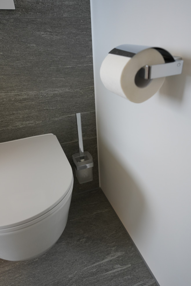 Duschbad With flächenbündigen Schrankfronten, weißen Schränken, bodengleicher Dusche, Wandtoilette, weißen Fliesen, Steinfliesen, Wandwaschbecken, Mineralwerkstoff-Waschtisch, grauem Boden, Falttür-Duschabtrennung, weißer Waschtischplatte, Einzelwaschbecken and schwebendem Waschtisch in Munich