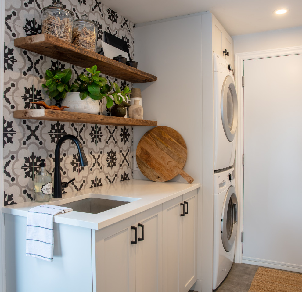 Small traditional single-wall dedicated laundry room in Ottawa with a single-bowl sink, shaker cabinets, white cabinets, quartz benchtops, multi-coloured splashback, porcelain splashback, multi-coloured walls, porcelain floors, a stacked washer and dryer, grey floor and white benchtop.