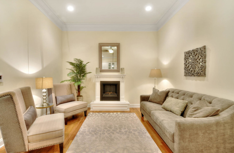 This is an example of a transitional living room in New York with light hardwood floors, a standard fireplace, a wood fireplace surround and no tv.