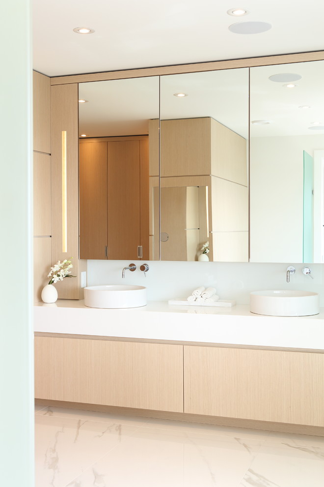 Design ideas for a large contemporary master bathroom in Vancouver with flat-panel cabinets, light wood cabinets, a freestanding tub, a corner shower, a one-piece toilet, white tile, glass sheet wall, white walls, ceramic floors, a vessel sink, engineered quartz benchtops, beige floor, a hinged shower door and white benchtops.