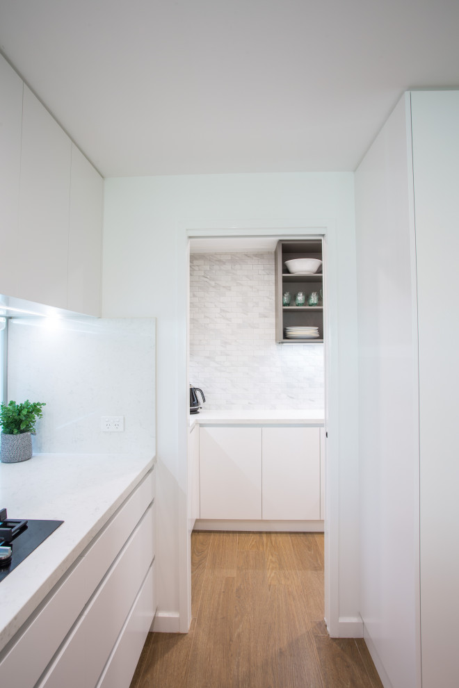 This is an example of a large modern u-shaped kitchen pantry in Brisbane with a drop-in sink, flat-panel cabinets, white cabinets, quartz benchtops, white splashback, black appliances, porcelain floors, with island, brown floor and white benchtop.