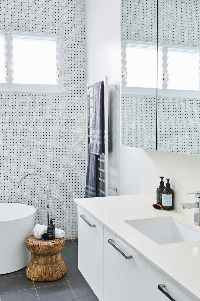 Inspiration for a mid-sized contemporary bathroom in Sydney with flat-panel cabinets, white cabinets, a freestanding tub, white tile, white walls, an undermount sink and black floor.
